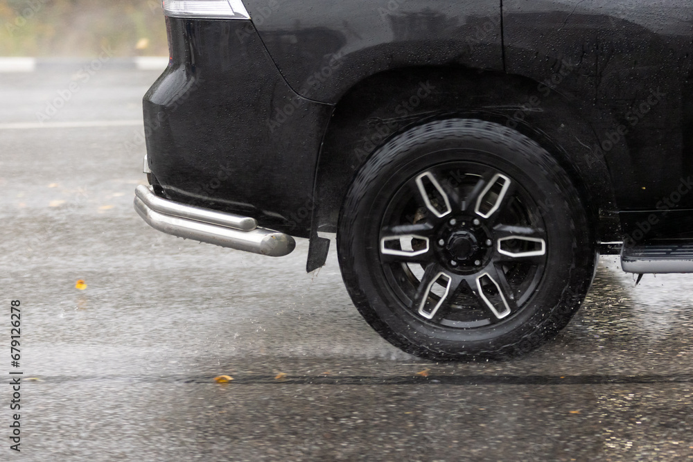 rain water splashing flows from wheels of black car that moving fast on asphalt road