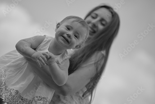 Mother lifts joyous baby in the air, under a tree canopy. Captures the joy of parenting and nature's embrace. photo