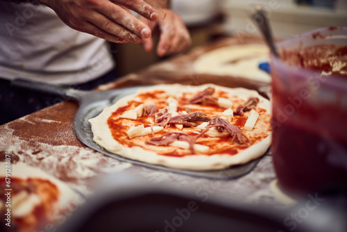 Close-up of a male putting ingredients on the pizza dough, making a Napoletana pizza.