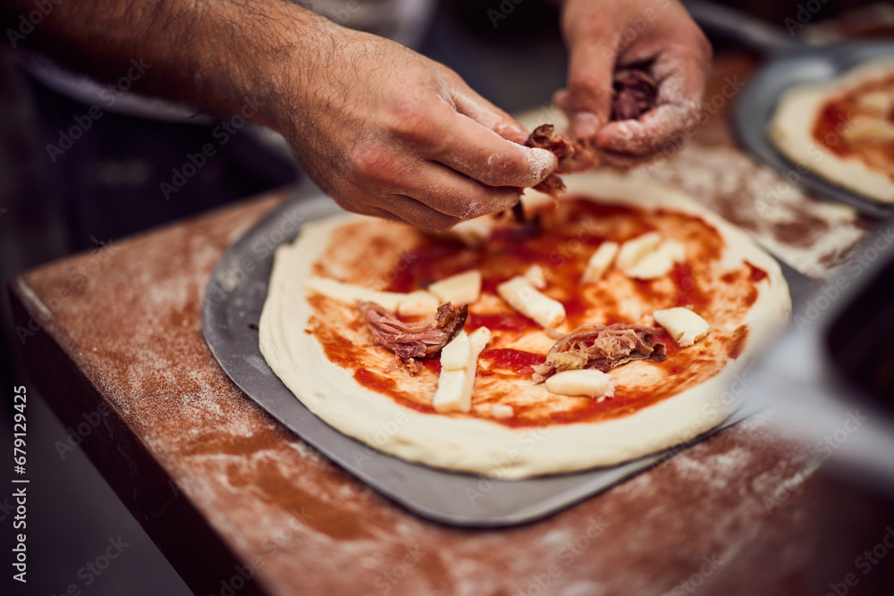 The male hands put ingredients on the pizza dough, preparing it on the pizza shovel.