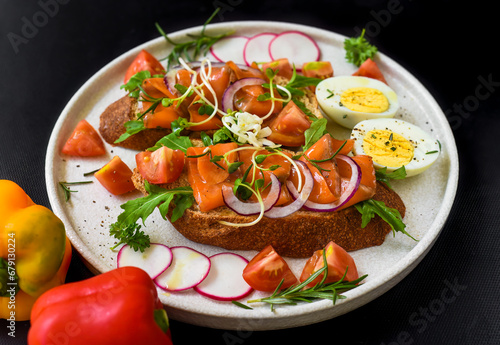 toast with smoked salmon, onion and vegetables on a white plate close up