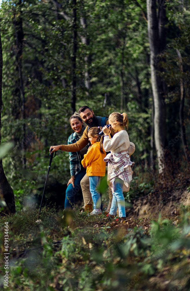Fototapeta premium Smiling family of four enjoying hiking in trough forest using binoculars.