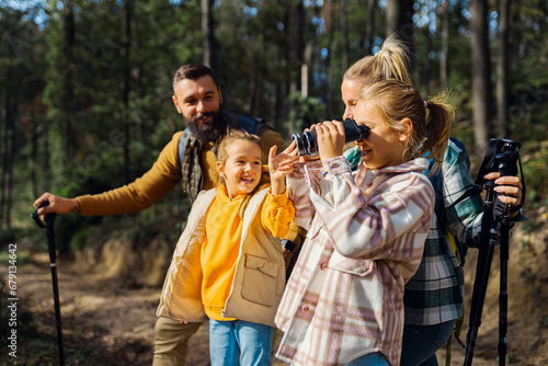 Smiling family of four enjoying hiking in trough forest using binoculars.