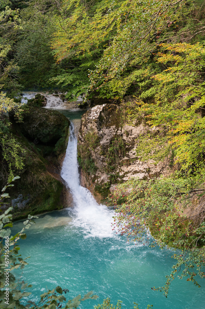 Paisaje otoñal de una cascada en el nacedero del río Urederra en la sierra de Urbasa con hayas y el agua del río, Navarra, España.