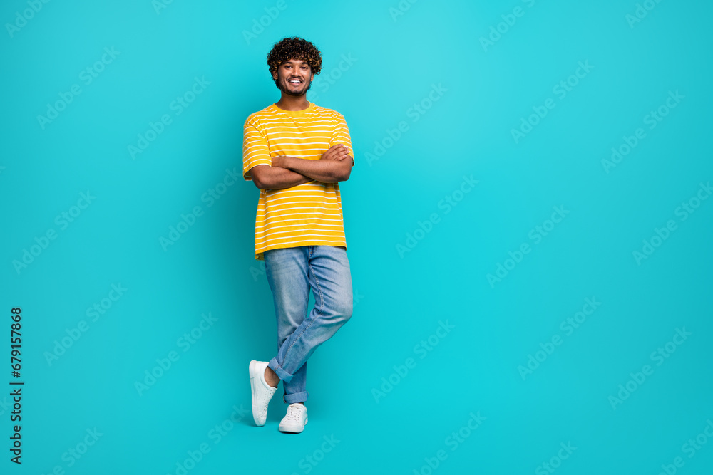 Full size photo of attractive young man folded arms posing wear trendy striped yellow clothes isolated on aquamarine color background Full size photo of attractive young man folded arms posing wear trendy striped yellow clothes isolated on aquamarine color background