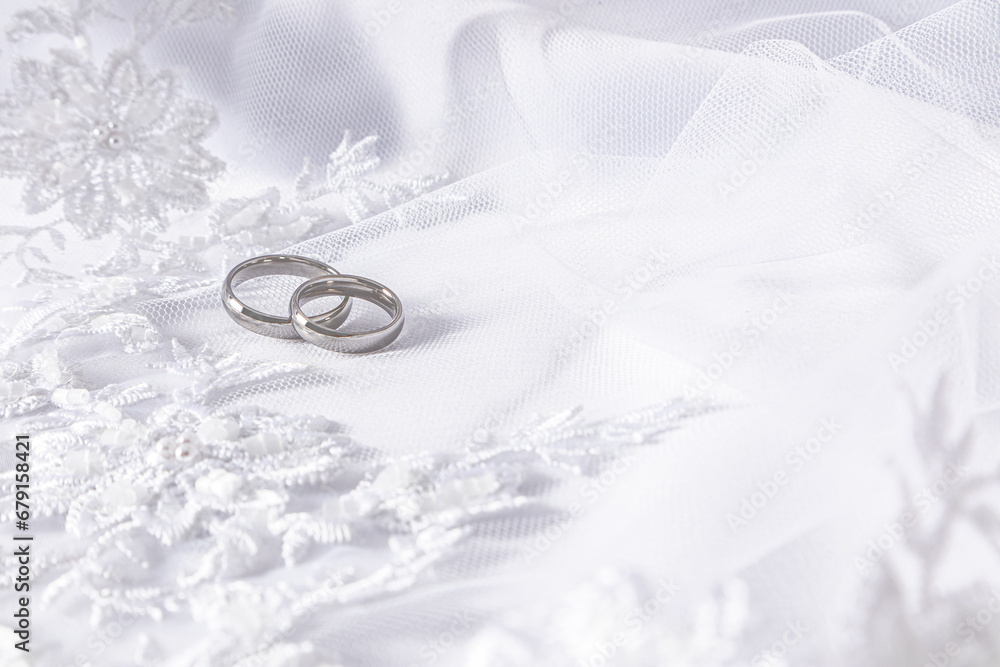 Two classic wedding rings in white gold against a white beader and pearl bridal veil. A copy of the space. Selective focus. Two classic wedding rings in white gold against a white beader and pearl bridal veil. A copy of the space. Selective focus.