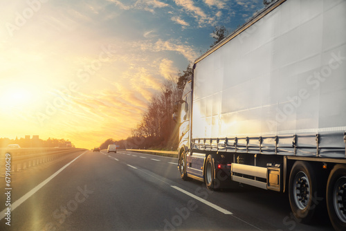 Tail view white blank modern delivery big shipment cargo commercial semi trailer truck moving motorway road city urban suburb. Business distribution logistics service. Lorry driving highway sunset photo