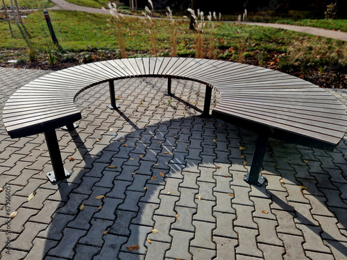 circular bench made of brown-red teak wood. tropical impregnated boards for sunbathing visitors in the park. spiral shape, snail shells. trowel base in lawn, tree, trunk, grass photo