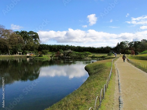 Woman on a path next to Lake with clear reflection of blue sky and clouds, representing: future, journey, satisfaction, retirement, peaceful life