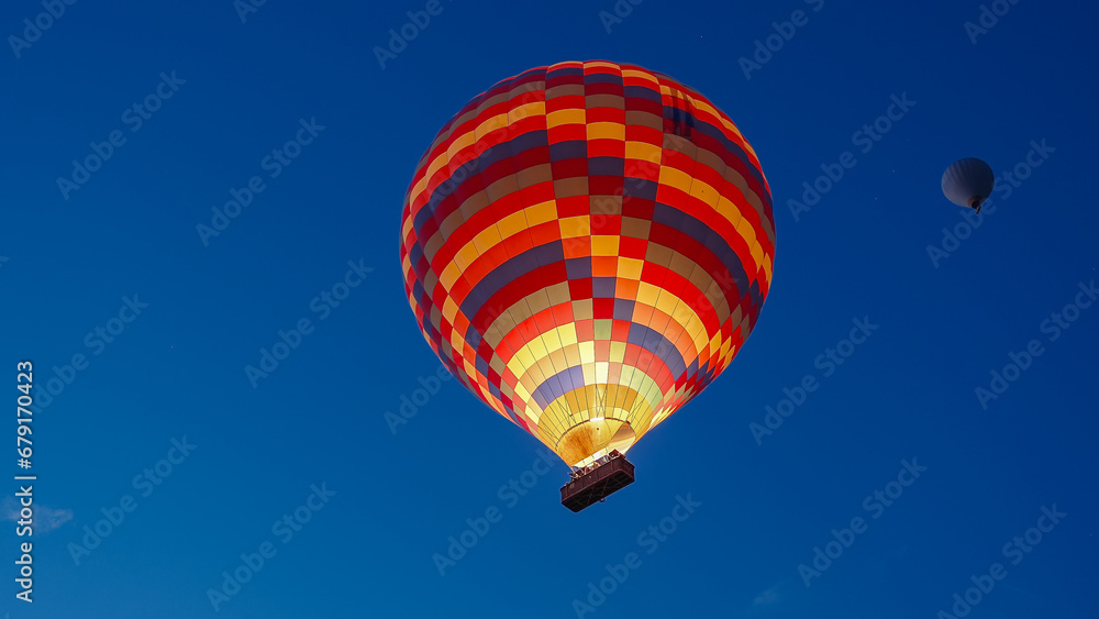 Fototapeta premium A multicolored hot air balloon with people in the basket, against the dark sky at dawn. Fire burns inside.