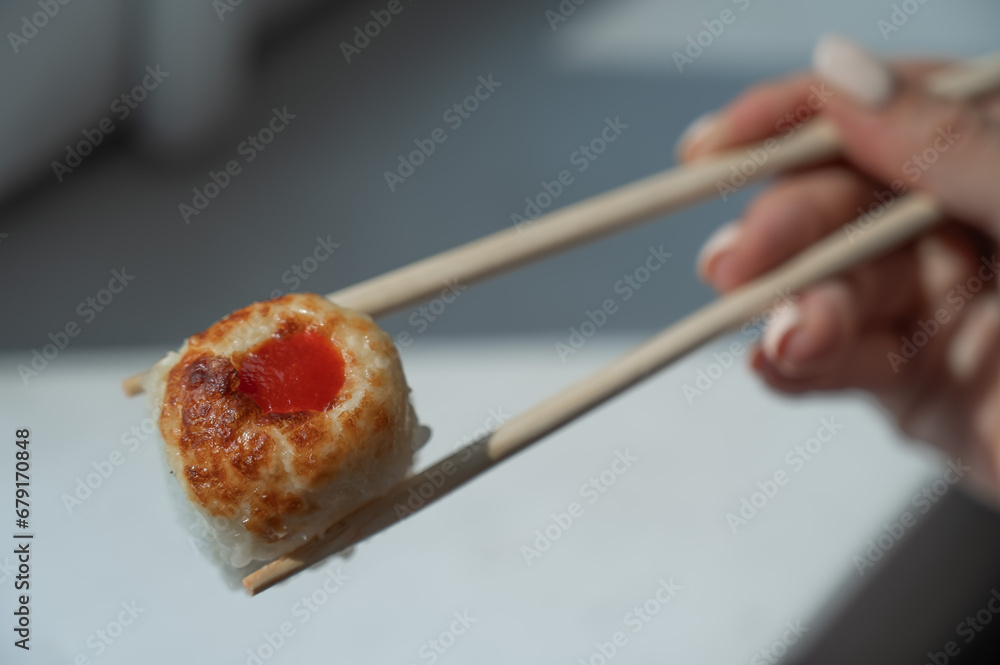 A woman holds a roll with chopsticks. Close-up of a woman's hand with Japanese food.