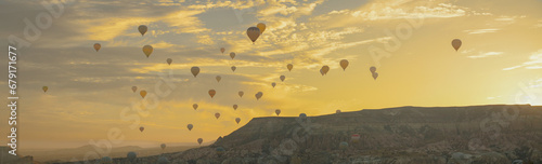 The valley with hot air balloons at sunrise amid the rocks, the sun rising from behind the mountains painted the clouds in golden color, Cappadocia, Turkey.