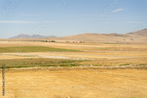Hills and mountains on a barren, scorched grassland. Clear blue sky overhead.