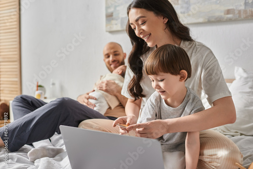 focus on joyous mother with her little son looking at laptop holding credit card, family concept