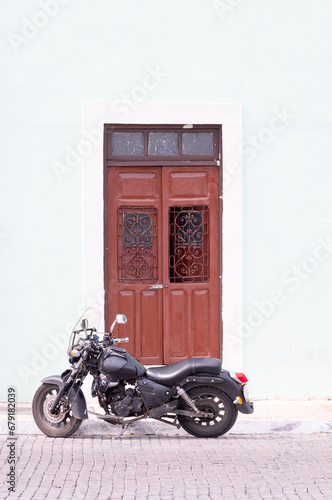 A beautiful motorcycle parked in front of an old street brown gate - Mexico