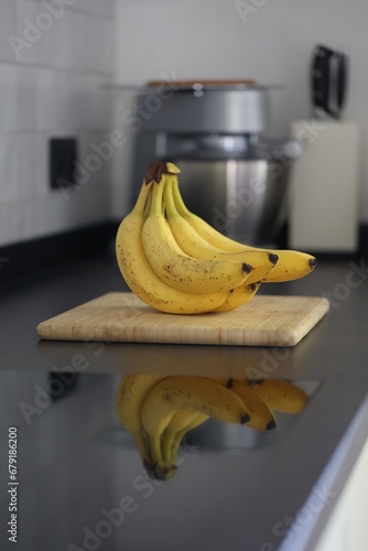A portrait of a bunch of yellow bananas lying on a wooden cutting board on a black kitchen countertop. The delicious energizing food is ready to eat and ideal before sport.