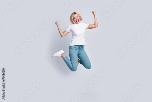 Full length photo of ecstatic satisfied girl wear stylish t-shirt jeans jumping clenching fists win bet isolated on gray color background