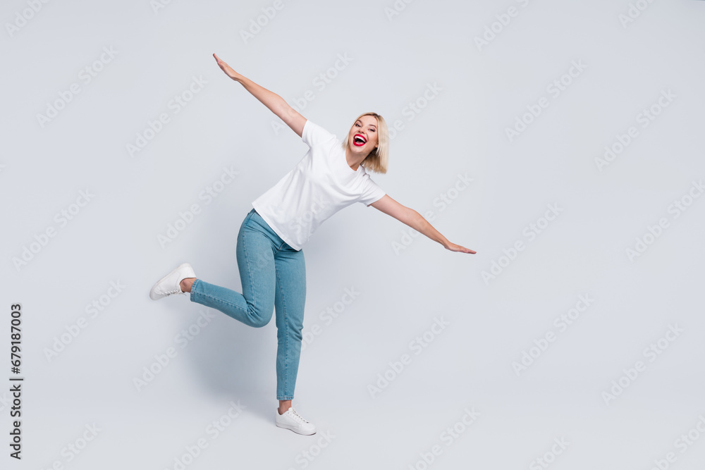 Full body photo of funny childish woman with short hairstyle wear stylish t-shirt hold palms like wings isolated on gray color background
