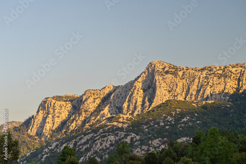 Rocks and mountains with sparse shrubs on the top illuminated by the setting sun.