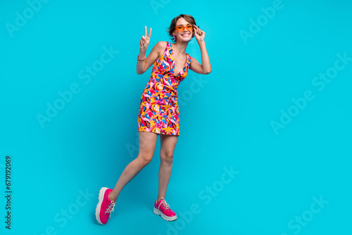 Full length photo of shiny cool girl dressed print outfit dark eyewear showing v-sign isolated blue color background