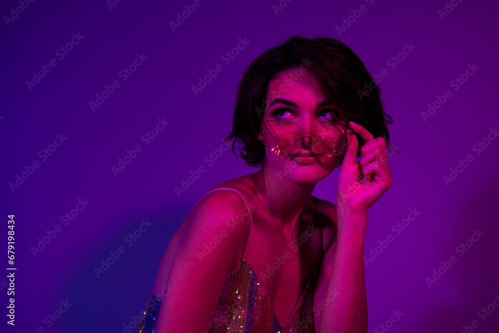 Photo of cool young woman wear sunglass heart shape spectacles looking dreamy coquettish empty space isolated over on neon light background Photo of cool young woman wear sunglass heart shape spectacles looking dreamy coquettish empty space isolated over on neon light background