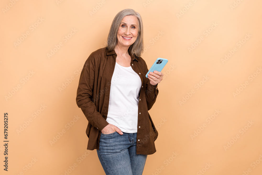 Portrait of toothy beaming person with bob hairdo wear stylish jacket hand in pocket hold smartphone isolated on beige color background Portrait of toothy beaming person with bob hairdo wear stylish jacket hand in pocket hold smartphone isolated on beige color background