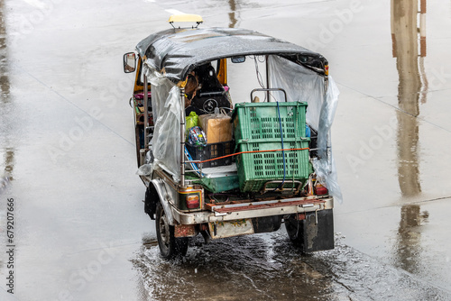 Taxi motor tricycle, tuk tuk, loaded with cargo is drives on the street in the rain, Bangkok, Thailand photo