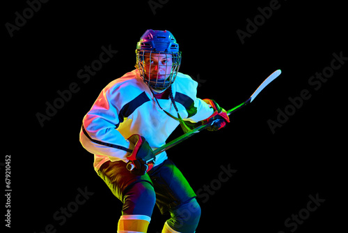 Concentrated, motivated young girl, hockey player standing in uniform with stick against black studio background in neon light. Concept of professional sport, competition, game, action, hobby © master1305
