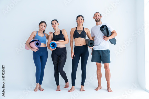 Group of three female friends and a man wearing exercise clothes holding yoga mats preparing to do yoga exercises together in studio.Healthy lifestyle concept