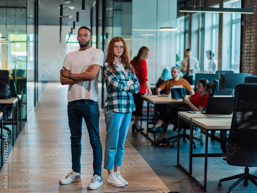 African-American businessman and his businesswoman colleague stand at the forefront with crossed arms, exuding confidence and leadership, while their diverse team diligently works behind them