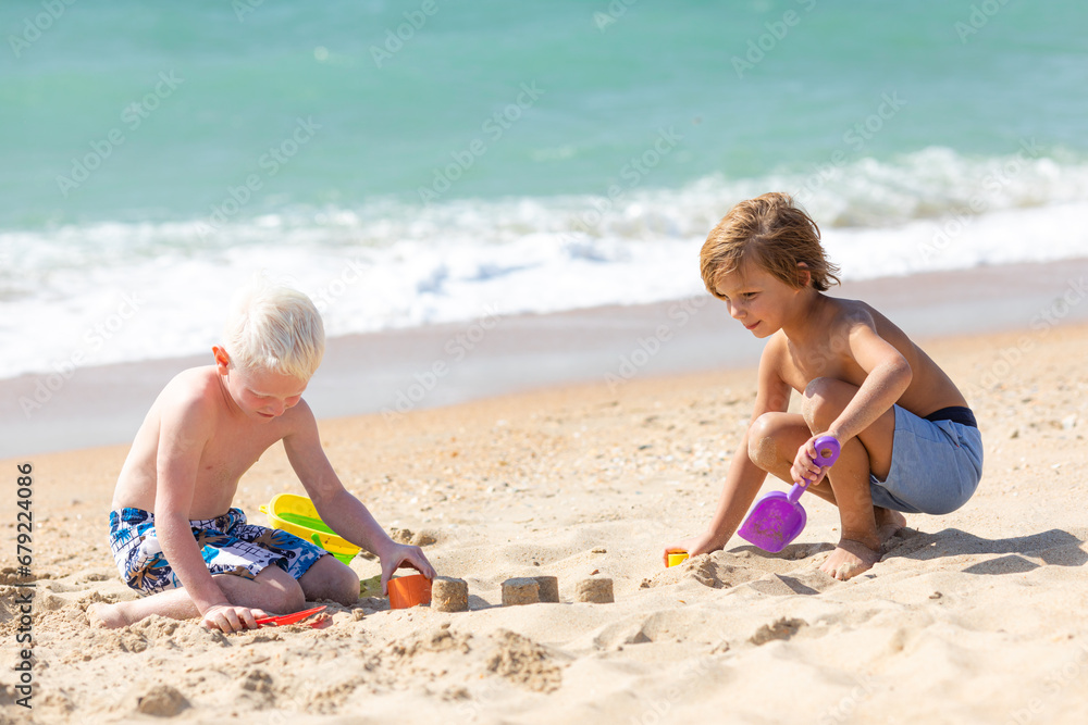 Children two little boys playing on the beach on summer holidays. Children having fun with a sand on the seashore. Vacation concept. Happy sunny day. Joyful children with beautiful sea, sand Children two little boys playing on the beach on summer holidays. Children having fun with a sand on the seashore. Vacation concept. Happy sunny day. Joyful children with beautiful sea, sand