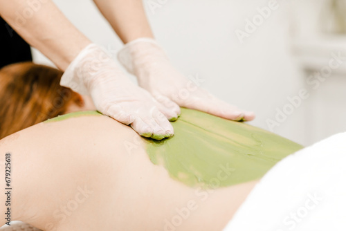 Woman receiving a therapeutic back massage with green algae, emphasizing relaxation and natural skincare treatment