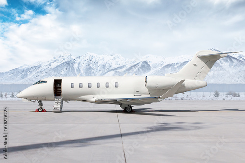 Modern white private jet with an opened gangway door at the winter airport apron on the background of high scenic snow capped mountains