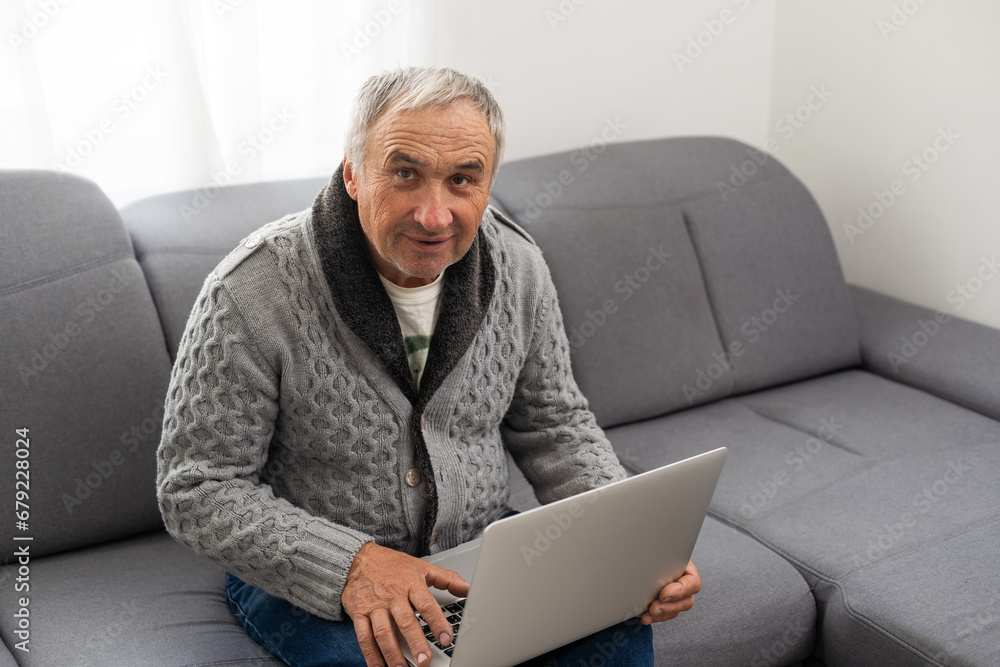 Older man sitting on sofa, smiling at computer screen at home Older man sitting on sofa, smiling at computer screen at home