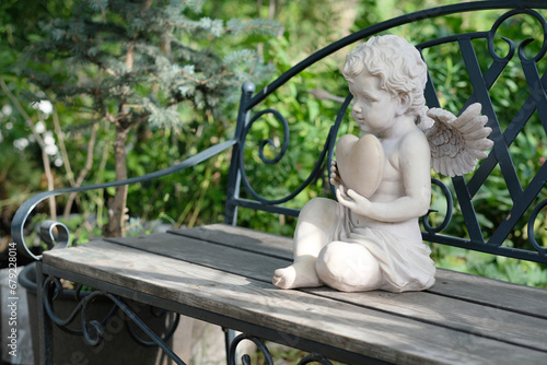Plaster figure of a thinking angel on a bench in summer