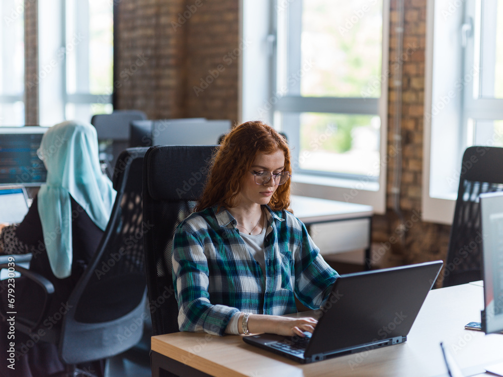 A young and successful businesswoman with vibrant orange hair engages in focused work within a modern office, showcasing her confidence and dynamic approach as she utilizes her laptop, emblematic of a A young and successful businesswoman with vibrant orange hair engages in focused work within a modern office, showcasing her confidence and dynamic approach as she utilizes her laptop, emblematic of a