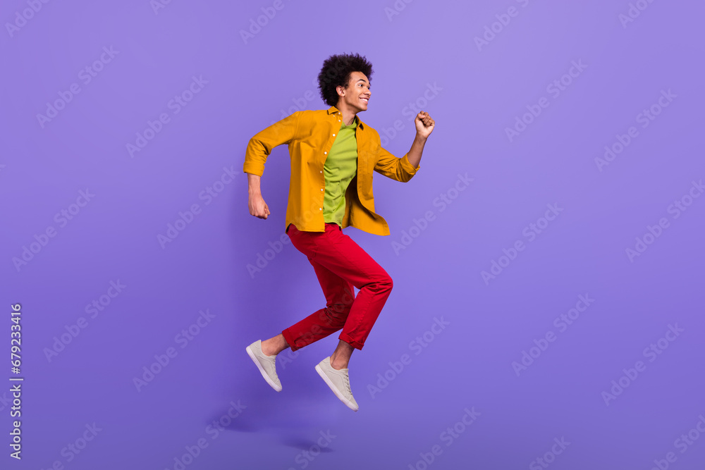 Full length profile side photo of cheerful glad man in trendy clothes going fast looking empty space isolated on purple color background Full length profile side photo of cheerful glad man in trendy clothes going fast looking empty space isolated on purple color background