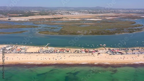 Aerial view of the ocean coast and beach. Boats on the water and tourists relaxing on the beach as seen from a drone. Praia de Faro Algarve Portugal. Bird's eye view altitude.