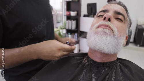 Client making faces while getting his beard shaped by stylist.MOV photo