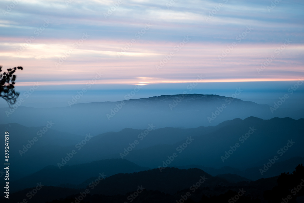 Fototapeta premium Golden sunset illuminates mountains, clouds, and a tranquil forest, casting a warm orange embrace over the serene landscape
