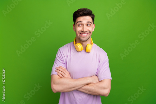 Portrait of funny person wear violet t-shirt clenching fist in headphones hands folded look empty space isolated on green color background
