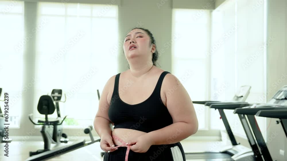 Chubby woman Exercise in fitness using a tape measure around waist. Face disappointed at not being able to lose weight to make waist smaller After running on the treadmill in attempt to lose weight Chubby woman Exercise in fitness using a tape measure around waist. Face disappointed at not being able to lose weight to make waist smaller After running on the treadmill in attempt to lose weight