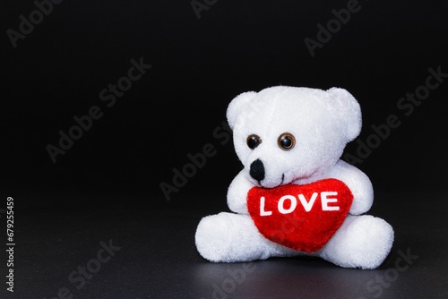 Plush teddy bear with a red heart in its hands on a dark background