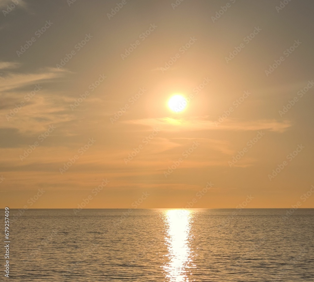 the sun rises over the ocean with a sailboat on the water