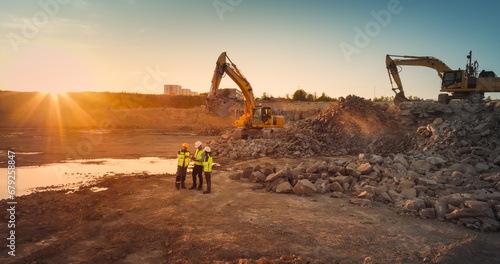 Aerial Drone Shot Of Construction Site With Excavators On Sunny Day: Diverse Team of Real Estate Developers Discussing Project. Civil Engineer, Architect, Inspector Talking And Using Tablet Computer.
