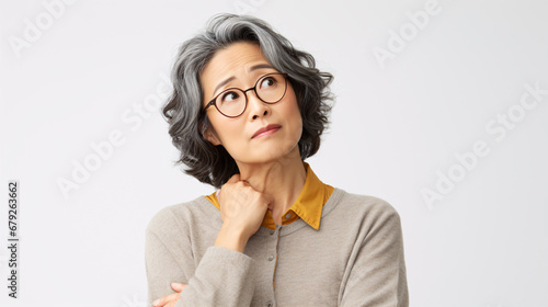 A baffled Japanese middle-aged woman, bewildered and exasperated, shrugging her shoulders and exhibiting a distressed countenance, inquires what is happening against a white backdrop.