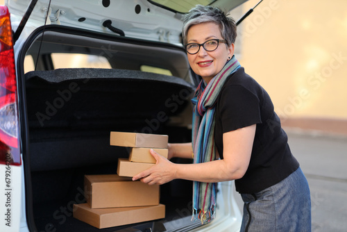 A confident and happy adult woman engaged in relocation, holding cardboard boxes, portraying positivity and excitement during the move to a new apartment.