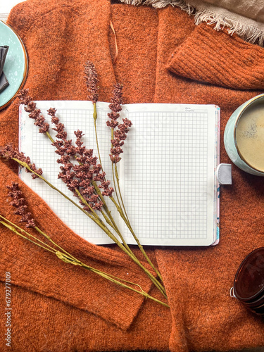 The image shows a notebook, cup of coffee, and flowers on a sweater. 
