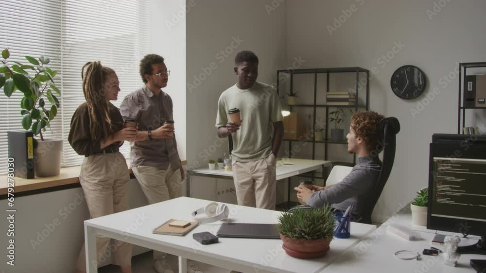 Four multiethnic male and female co-workers chatting during coffee break in contemporary programmers office Four multiethnic male and female co-workers chatting during coffee break in contemporary programmers office