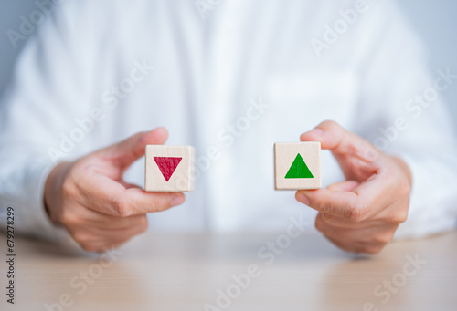Hand holding wood block with opposite direction arrow, red going down or green up arrow. Change of the finance interest rate and mortgage rates concept. Business inflation, sale price, loan, and tax. photo